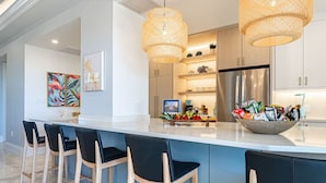 A modern kitchen with a large island, bar stools, and wicker pendant lights. - Luxe 3 BR: Beachfront Suite Next to Baha Mar (Nassau)