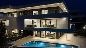 Une maison moderne à plusieurs étages, dotée d’une piscine, de grandes fenêtres et d’un balcon.