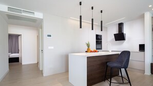 Une cuisine moderne dotée d’un îlot central, de luminaires suspendus noirs et d’un four encastré.