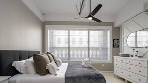 Une chambre à coucher comprenant un lit, une commode, un ventilateur de plafond et une fenêtre avec des stores.