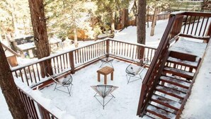Cubierta nevada con una escalera de madera, sillas de metal y una mesita.