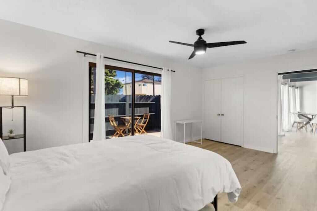 Un dormitorio con cama, ventilador de techo, ventana con vistas y puerta que da a un balcón.