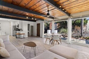 Amplia sala de estar con techo de madera, cocina al fondo y patio con mobiliario exterior.