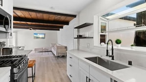 A modern kitchen with white cabinetry, a black stove, and a large window providing natural light. - Cozy, bright, and walk to Crown Point Park/Bay (San Diego)