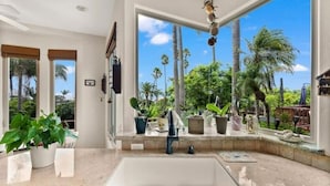 A kitchen with a large window, a sink, and various potted plants.