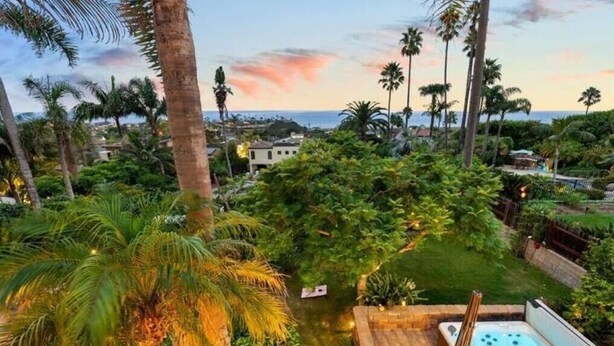 A lush garden with a hot tub and a view of the ocean at sunset.