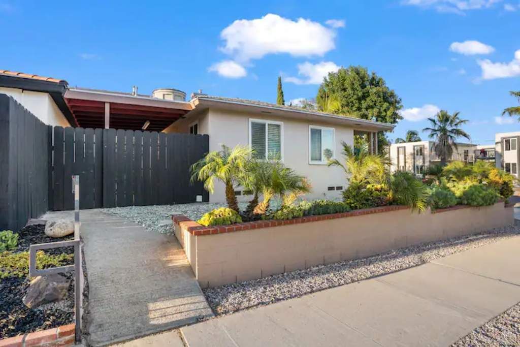 A modern house with a fenced backyard, a small patio, and a well-maintained garden with various plants and a palm tree.