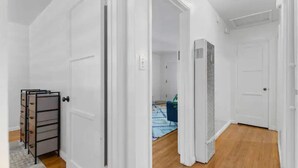 A hallway with white walls and wooden flooring, leading to a room with a bed and a blue chair. - Cozy, home with hottub & patio! (Los Angeles)