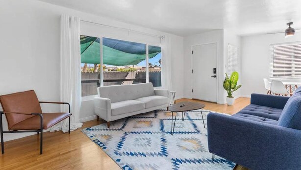 A modern living room with a sofa, a chair, a coffee table, and a view through large windows. - Cozy, home with hottub & patio! (Los Angeles)
