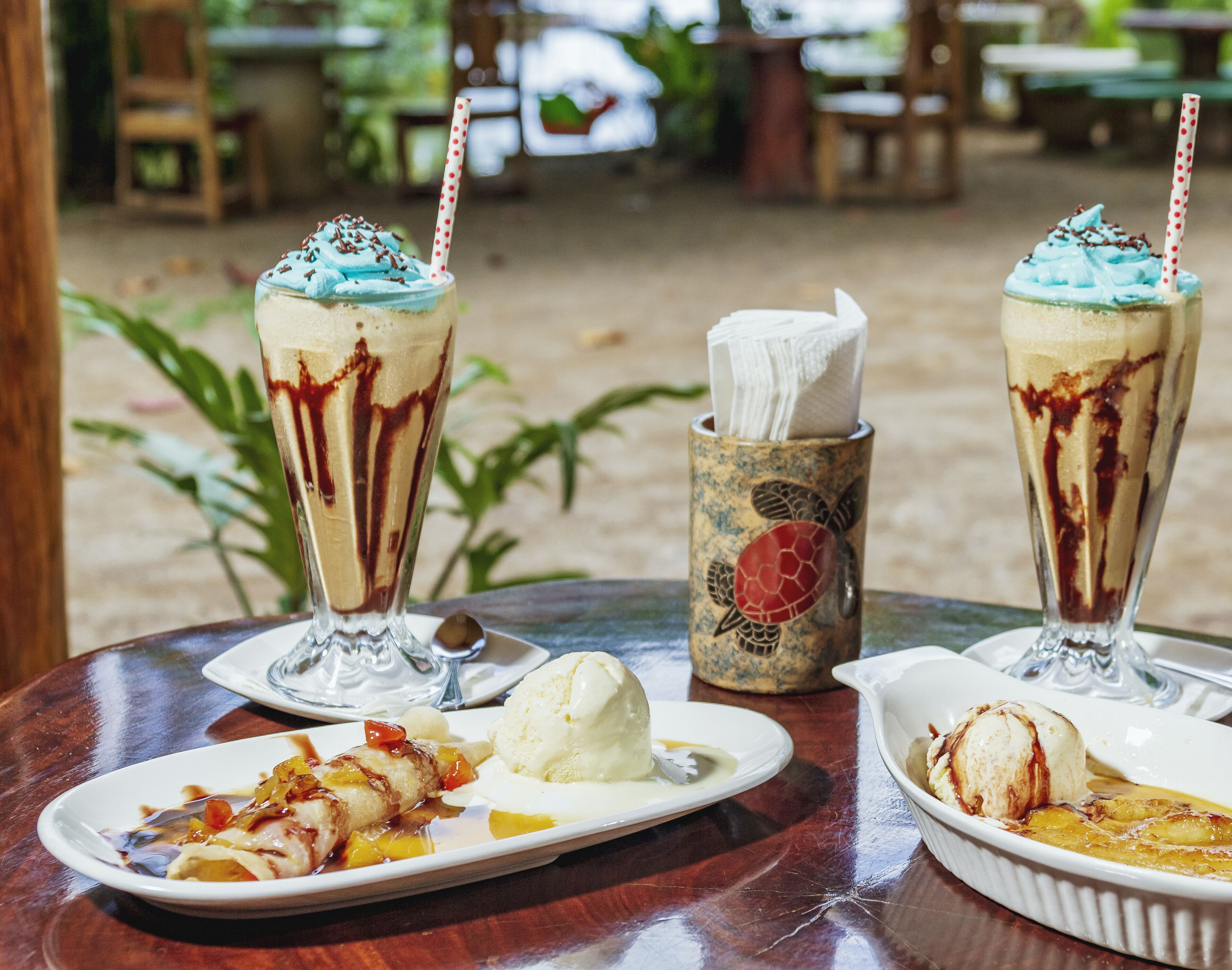 A table with two milkshakes, a plate of food, and a napkin holder.