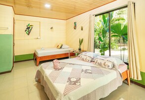 Una habitación con dos camas individuales, una mesita pequeña, una planta en maceta y una ventana con cortinas.