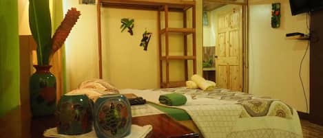 A bedroom with a wooden bed, a small desk with decorative items, a television, and a wardrobe.