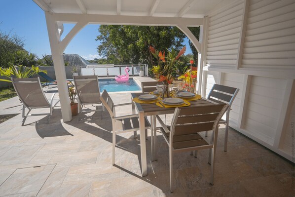 An outdoor patio with a table set for dining, surrounded by chairs, and a pool with a pink flamingo float.