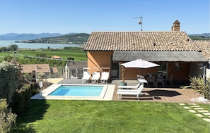 A villa with a swimming pool, outdoor seating, and a view of the lake and hills.