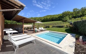 Una piscina con sillas de descanso, una pérgola y vistas a un paisaje verde.