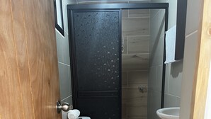 Une petite salle de bain compacte, équipée de toilettes, d’un lavabo et d’une porte noire.