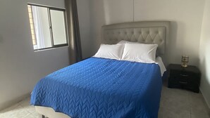 Une chambre à coucher avec un lit, une table de chevet, une fenêtre et un ventilateur de plafond.