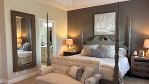 A bedroom with a four-poster bed, a tufted armchair, a large mirror, and a nightstand with a lamp. -  Pet friendly with community pool! (St. Simons Island)