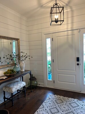 A hallway with a white door, a mirror, a bench, a vase with green balls, and a hanging light fixture. -  Pet friendly with community pool! (St. Simons Island)