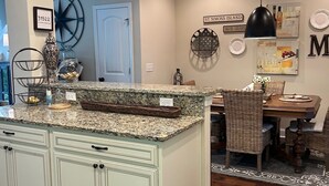 A kitchen with a granite countertop, white cabinetry, and a dining area with wicker chairs and a table. -  Pet friendly with community pool! (St. Simons Island)
