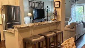A modern kitchen with a central island, bar stools, and a dining area with a sofa and a wicker chair. -  Pet friendly with community pool! (St. Simons Island)
