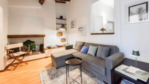 Un salon avec un canapé, une petite table ronde, un fauteuil de réalisateur, une bibliothèque et un miroir au mur.
