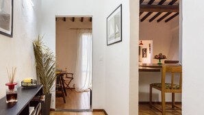 Un couloir avec un plancher en bois, une plante en pot, une table avec une bougie et une chaise.