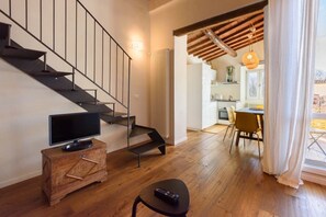 A modern interior with a staircase, a television on a wooden chest, a remote on a stool, and a dining area with chairs and a table. - Terrace on the roofs apartment in Florence by Mmega (Firenze)