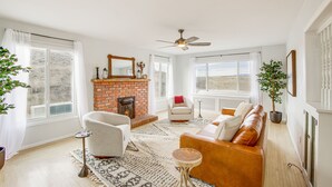 A living room with a brick fireplace, a ceiling fan, and a large window. - Secluded Montana Getaway w/ Fire Pit & Views! (Ryegate)