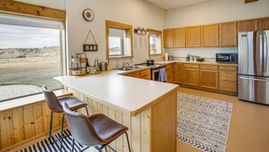 A kitchen with wooden cabinets, a stainless steel refrigerator, a large island with bar stools, and a view of the outdoors. - Secluded Montana Getaway w/ Fire Pit & Views! (Ryegate)