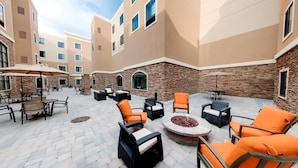 An outdoor patio area with multiple seating arrangements, including tables and chairs, and a central fire pit.