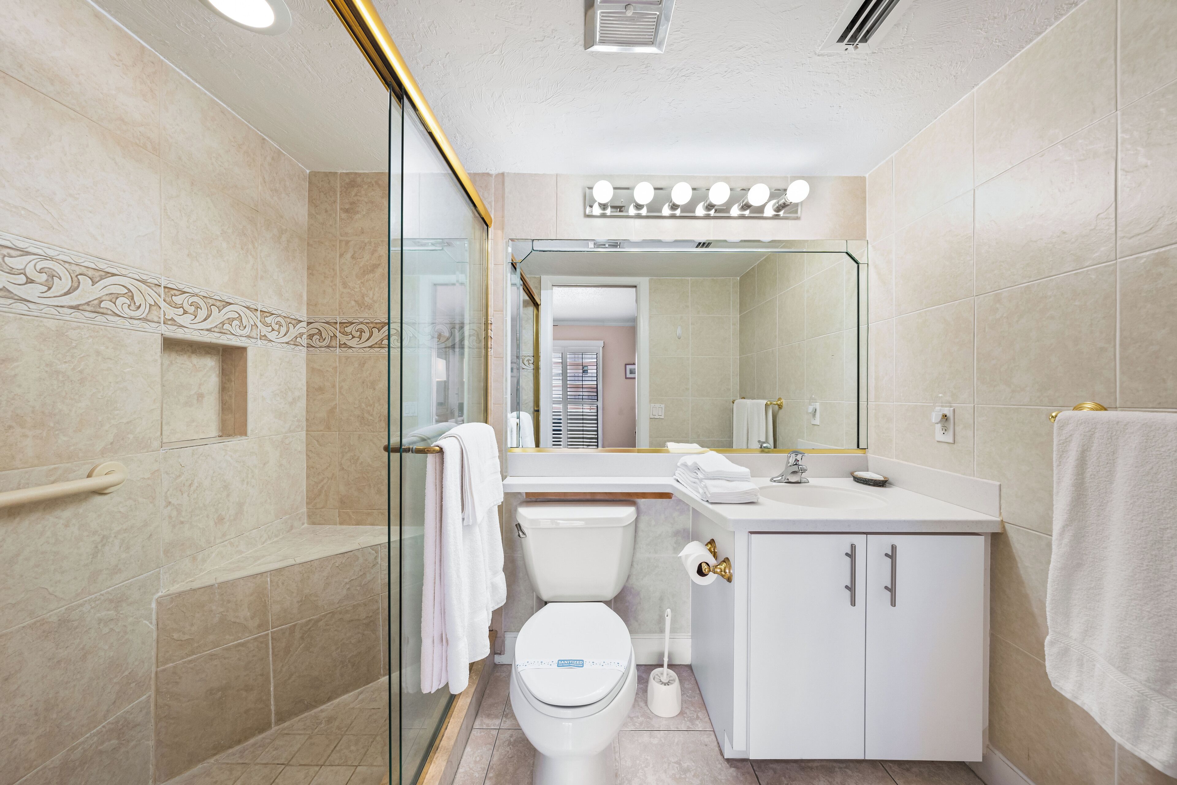 A modern bathroom with a glass shower enclosure, a white toilet, a vanity with a mirror, and a towel rack.