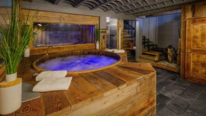 A wooden hot tub with a view of a stone wall and a wooden staircase.