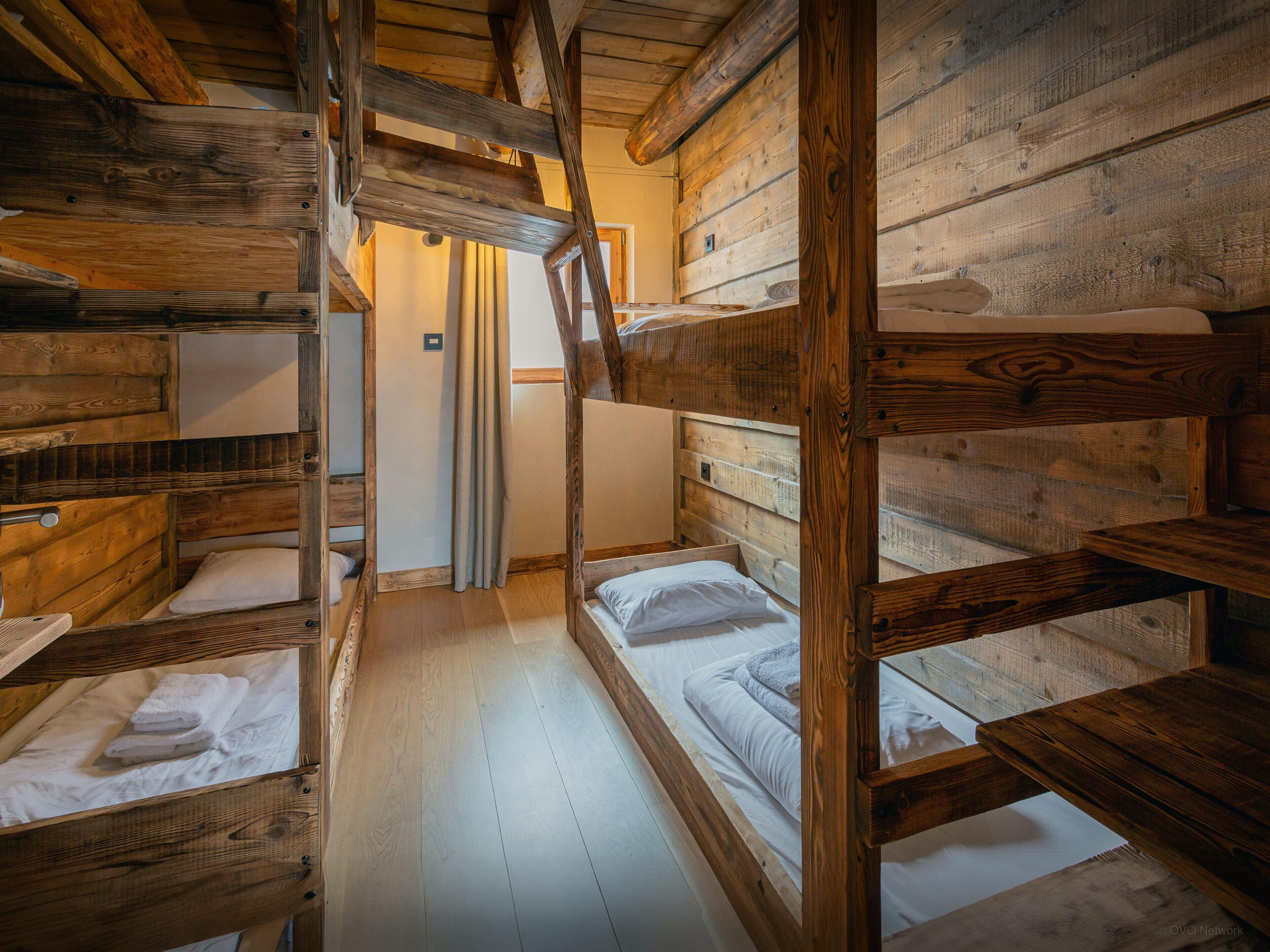 Una cabaña rústica de madera con literas, piso de madera y un diseño interior sencillo y funcional.