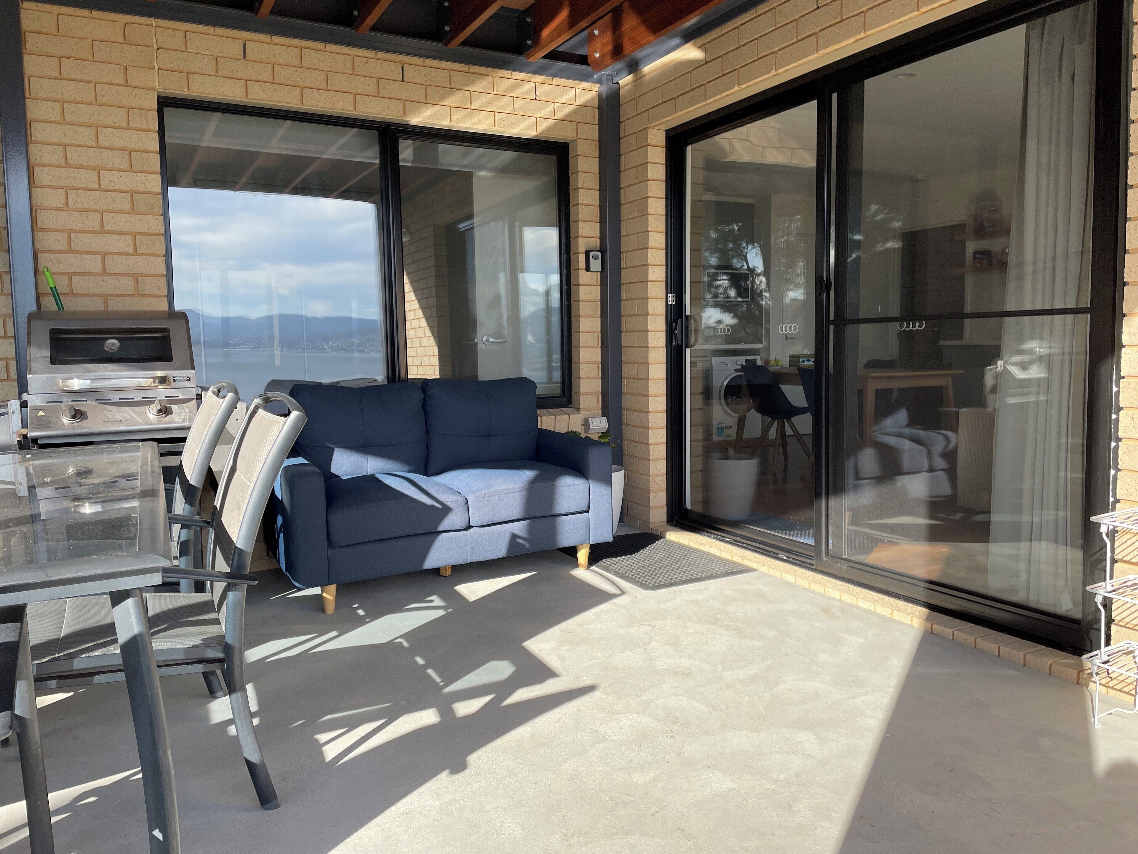 A modern outdoor living area with a glass door leading to a patio, a barbecue grill, and a blue sofa.