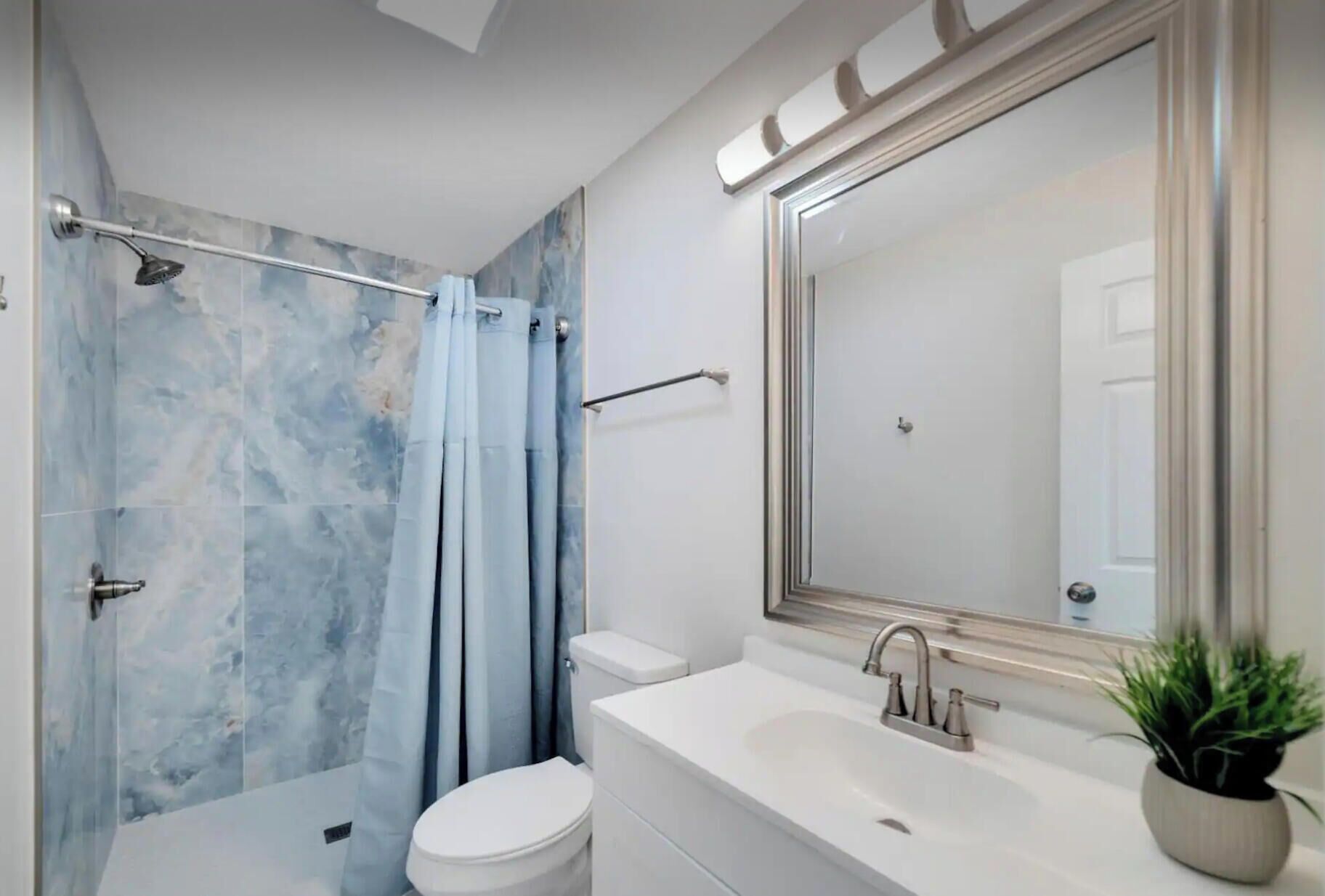 Un baño moderno con ducha, inodoro, lavabo y un espejo grande.