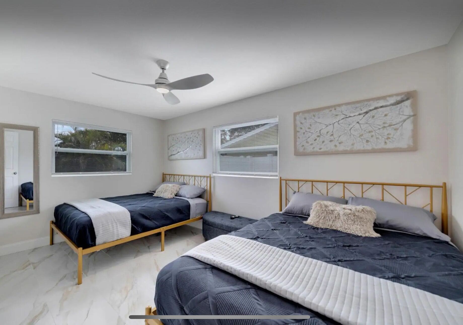 A bedroom with two beds, a ceiling fan, and artwork on the walls.