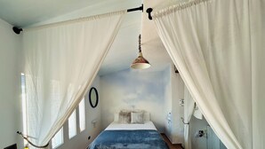 A bedroom with a bed, a bedside table, a hanging lamp, and a window with curtains.
