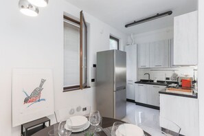 A modern kitchen with white cabinets, a stainless steel refrigerator, and a dining area with a table set for two.