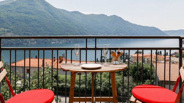 Un balcon avec une table et des chaises, donnant sur un lac et des montagnes.