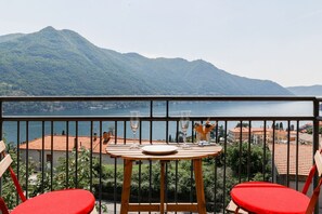 A balcony with a table and chairs, overlooking a lake and mountains.