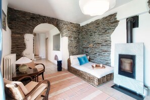 A room with a stone wall, a fireplace, wicker furniture, and a tiled floor.