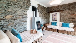 A stone-walled room with a fireplace, wicker furniture, and a hanging light fixture. - Lost in Paradise - My Home In Como (Santa Maria Rezzonico)