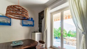A dining area with a table, chairs, a wicker hanging light fixture, a stone wall, and a view through a glass door to an outdoor patio. - Lost in Paradise - My Home In Como (Santa Maria Rezzonico)
