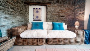 A stone-walled room with a wicker sofa and cushions, a wall-mounted decorative piece, and a lamp. - Lost in Paradise - My Home In Como (Santa Maria Rezzonico)