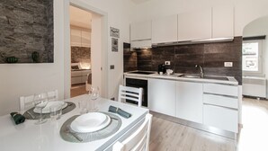 Uma cozinha moderna com armários brancos, painel de fundo escuro e um espaço de refeições com mesa posta para dois.