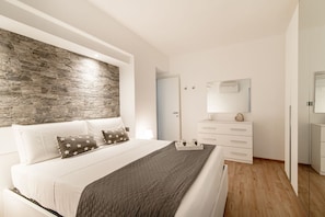 Un dormitorio moderno con una pared de acento de piedra, una cama con almohadas estampadas con motivos de estrellas, una mesita de noche con lámpara y un aparador con cajones.