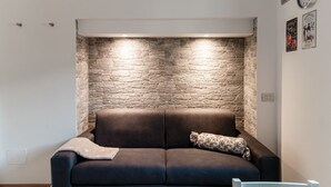 Uma sala de estar moderna com uma parede de destaque em pedra, um sofá marrom escuro e uma mesinha.