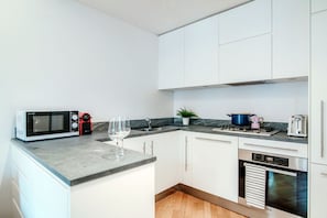 Une cuisine moderne avec des meubles blancs, un four à micro-ondes, une machine à café rouge, un verre de vin, une cuisinière et un grille-pain.