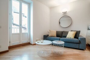 Habitació amb un sofà, dues taules rodones, un mirall i una porta que dona a un balcó.
